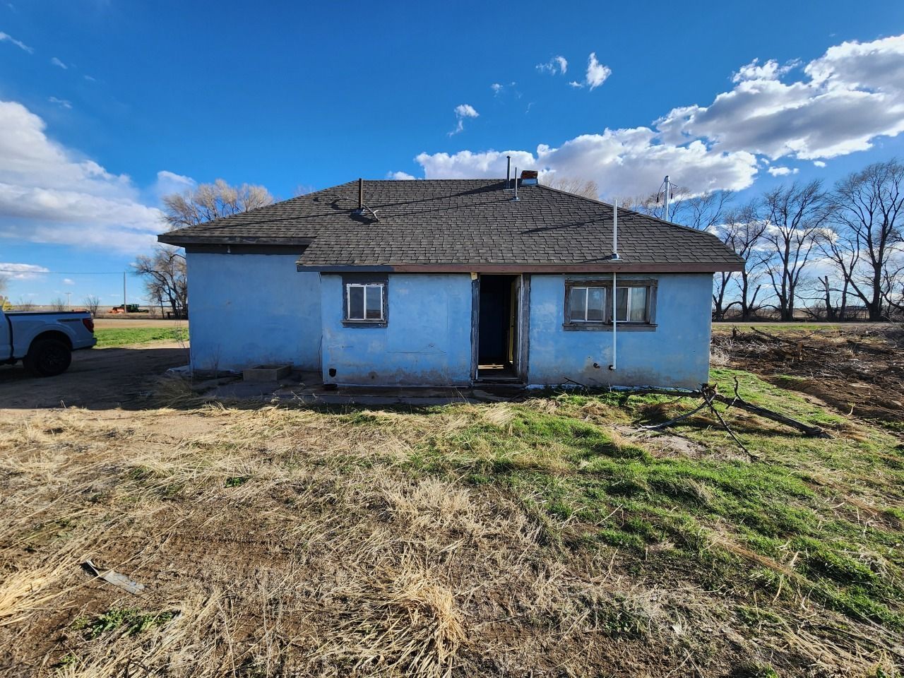 Small blue rural house with a tiled roof under a bright sky, surrounded by dry grass. Small blue rural house with a tiled roof under a bright sky, surrounded by dry grass.