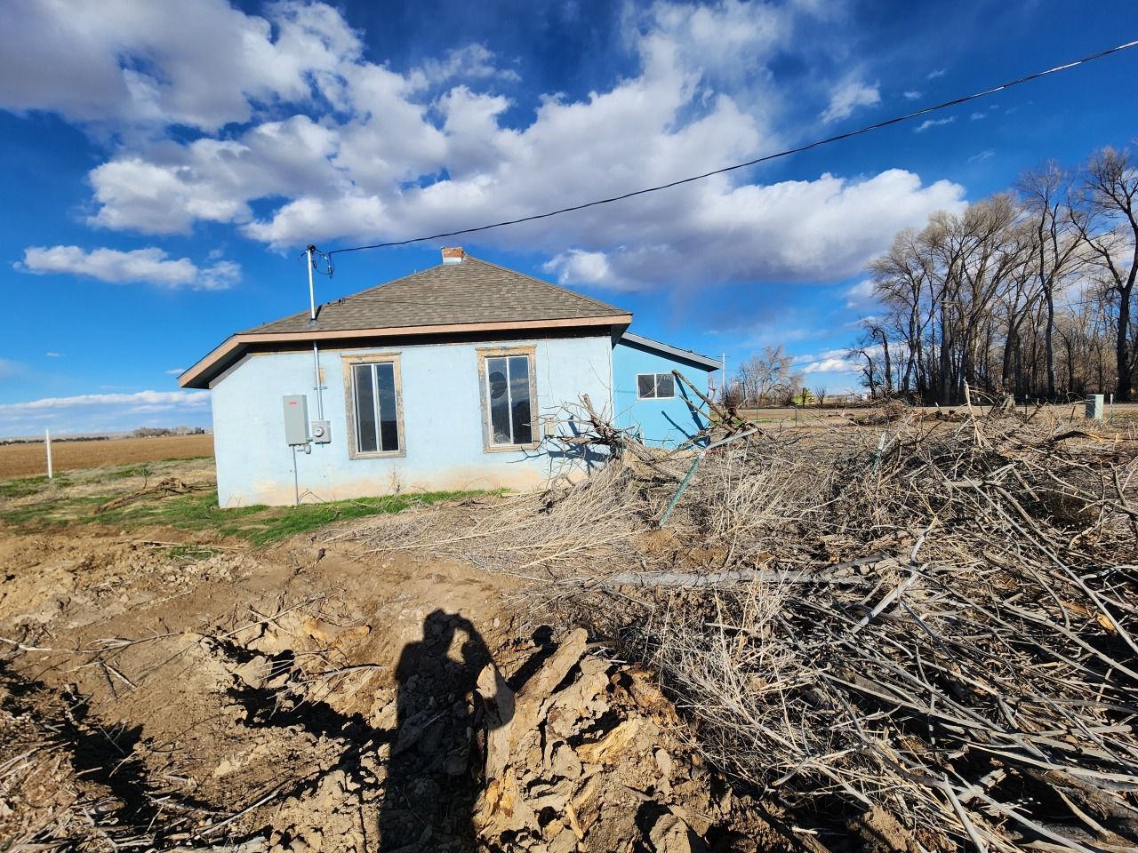 Small blue house beside a deep dirt trench, with brush piles and open fields under a cloudy sky. Small blue house beside a deep dirt trench, with brush piles and open fields under a cloudy sky.
