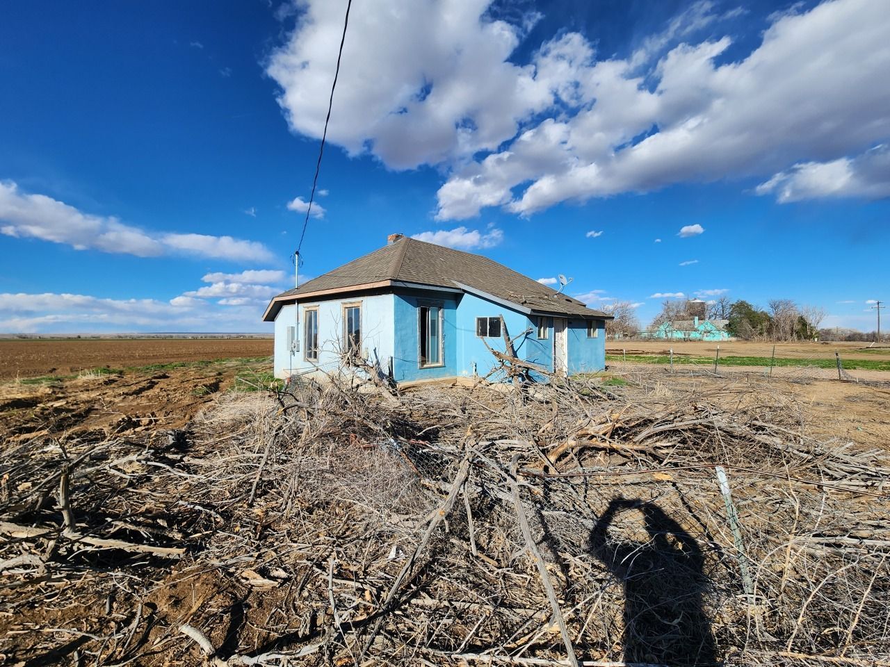 Small blue house in a dry field under a bright cloudy sky Small blue house in a dry field under a bright cloudy sky