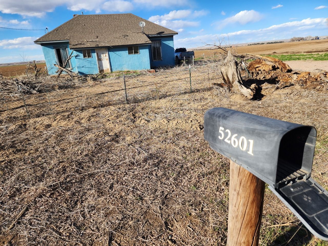 Blue house in a dry field with a black mailbox labeled 52601 in the foreground.