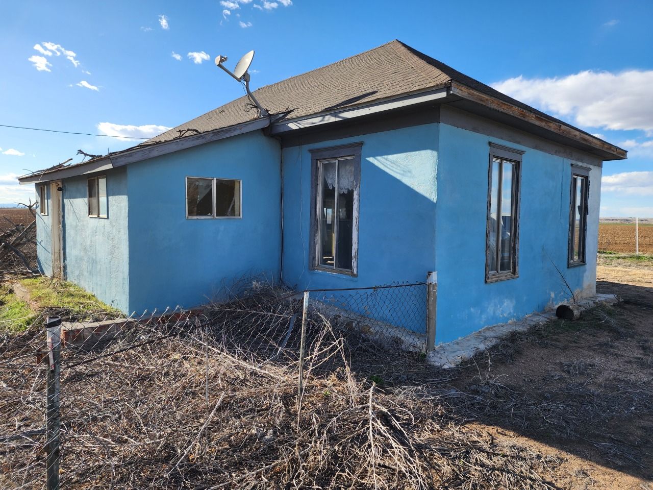 Blue single-story house with a gray roof in a bare yard under a clear sky Blue single-story house with a gray roof in a bare yard under a clear sky