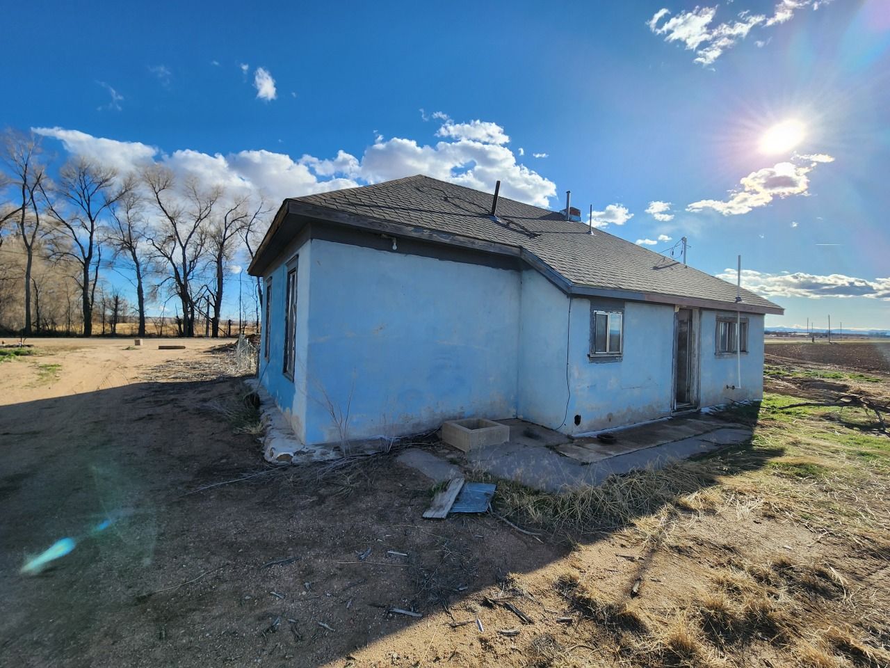 Small blue house with a gray roof in a sunny, open rural field under a partly cloudy sky. Small blue house with a gray roof in a sunny, open rural field under a partly cloudy sky.