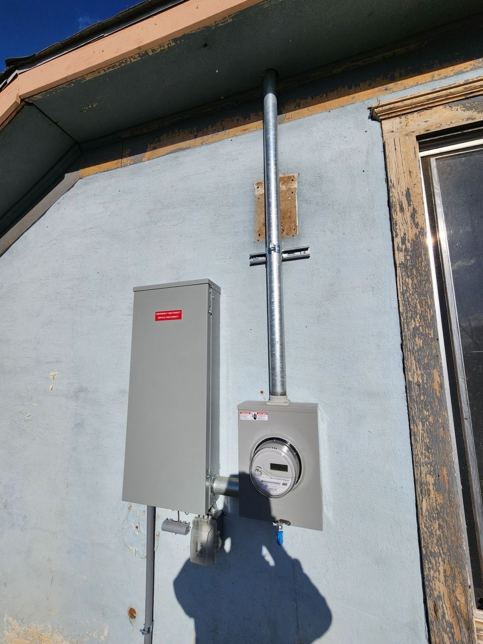 Outdoor electric meter and gray utility box mounted on a house wall.