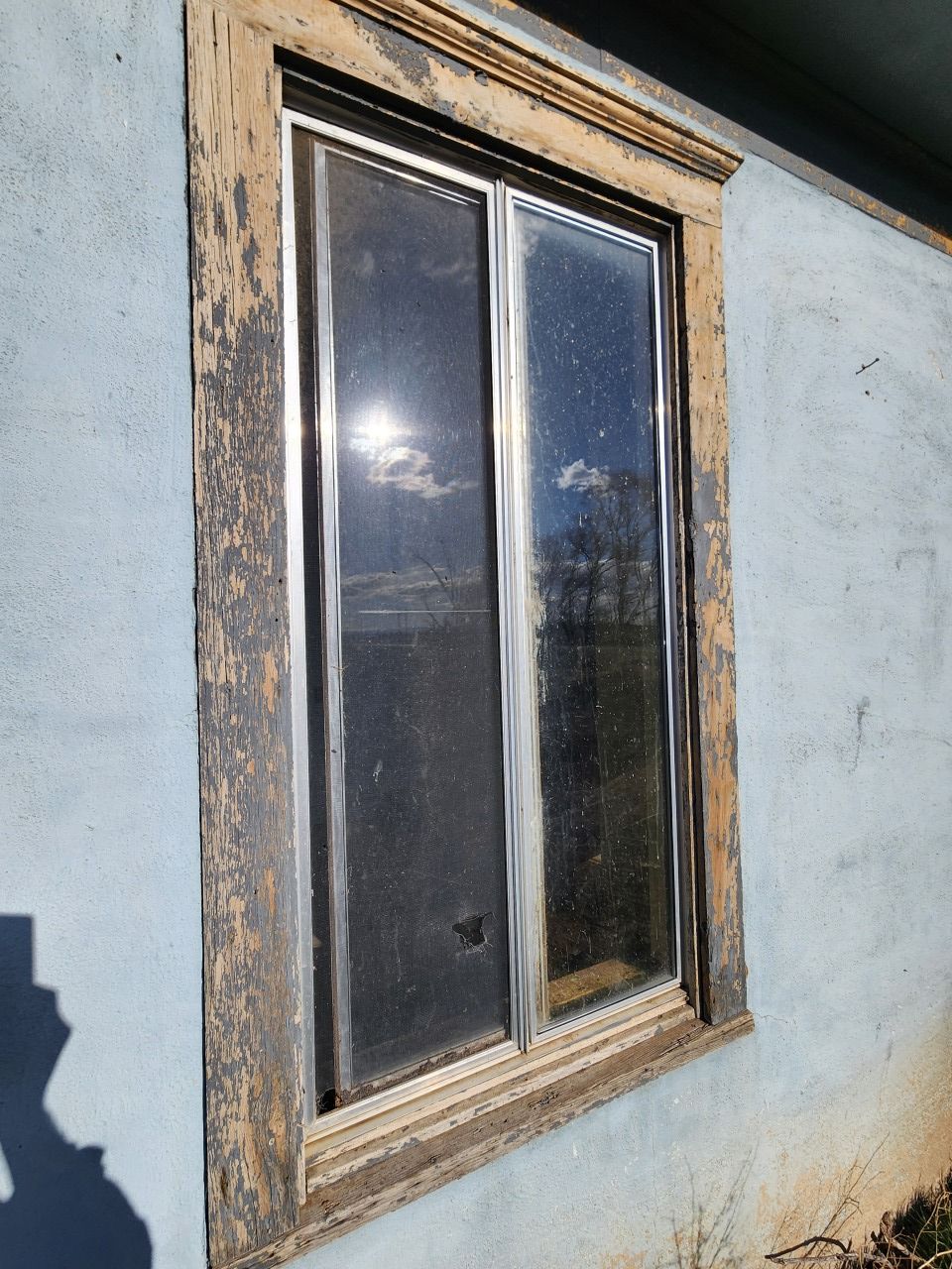 Weathered wooden-framed window on a blue exterior wall, reflecting sunlight. Weathered wooden-framed window on a blue exterior wall, reflecting sunlight.