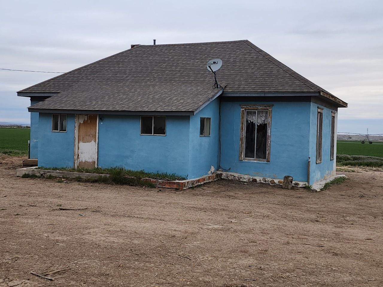 Small blue house with a damaged window and white door in a barren, open landscape Small blue house with a damaged window and white door in a barren, open landscape