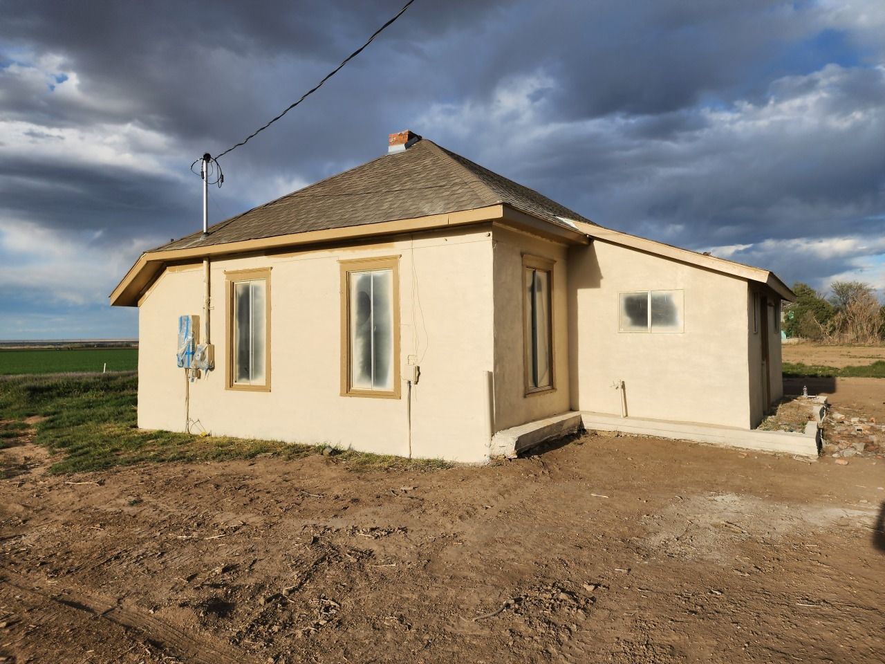Small beige house with a brown roof on a dirt lot under a cloudy sky. Small beige house with a brown roof on a dirt lot under a cloudy sky.
