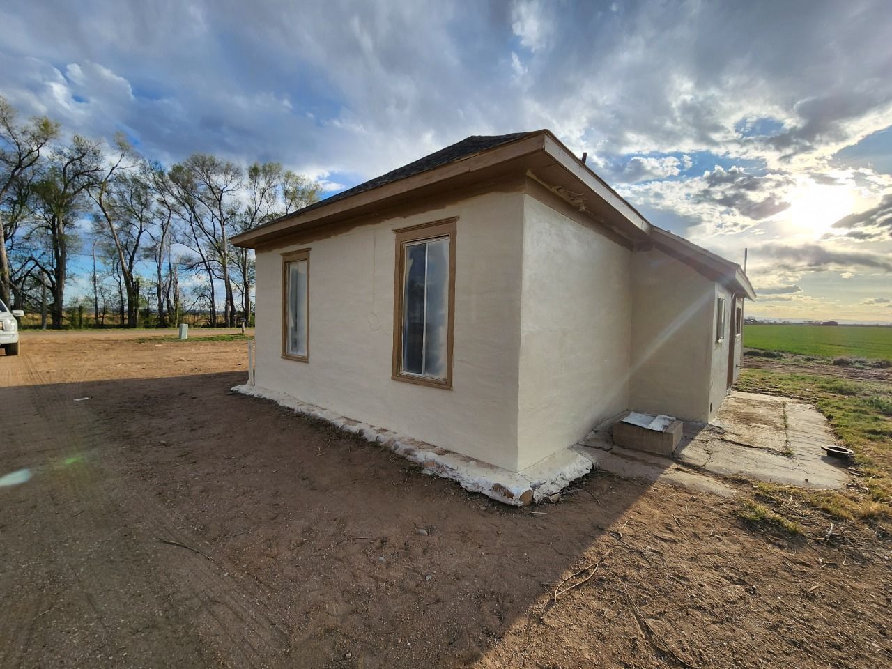 Small cream-colored house with brown roof in a rural field under a partly cloudy sky Small cream-colored house with brown roof in a rural field under a partly cloudy sky