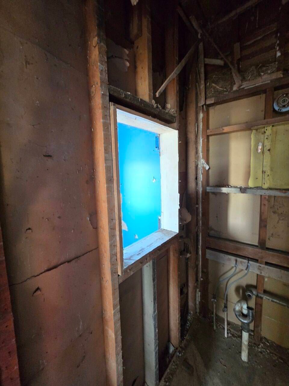 Unfinished wall framing around a bright blue window opening inside a room under construction Unfinished wall framing around a bright blue window opening inside a room under construction