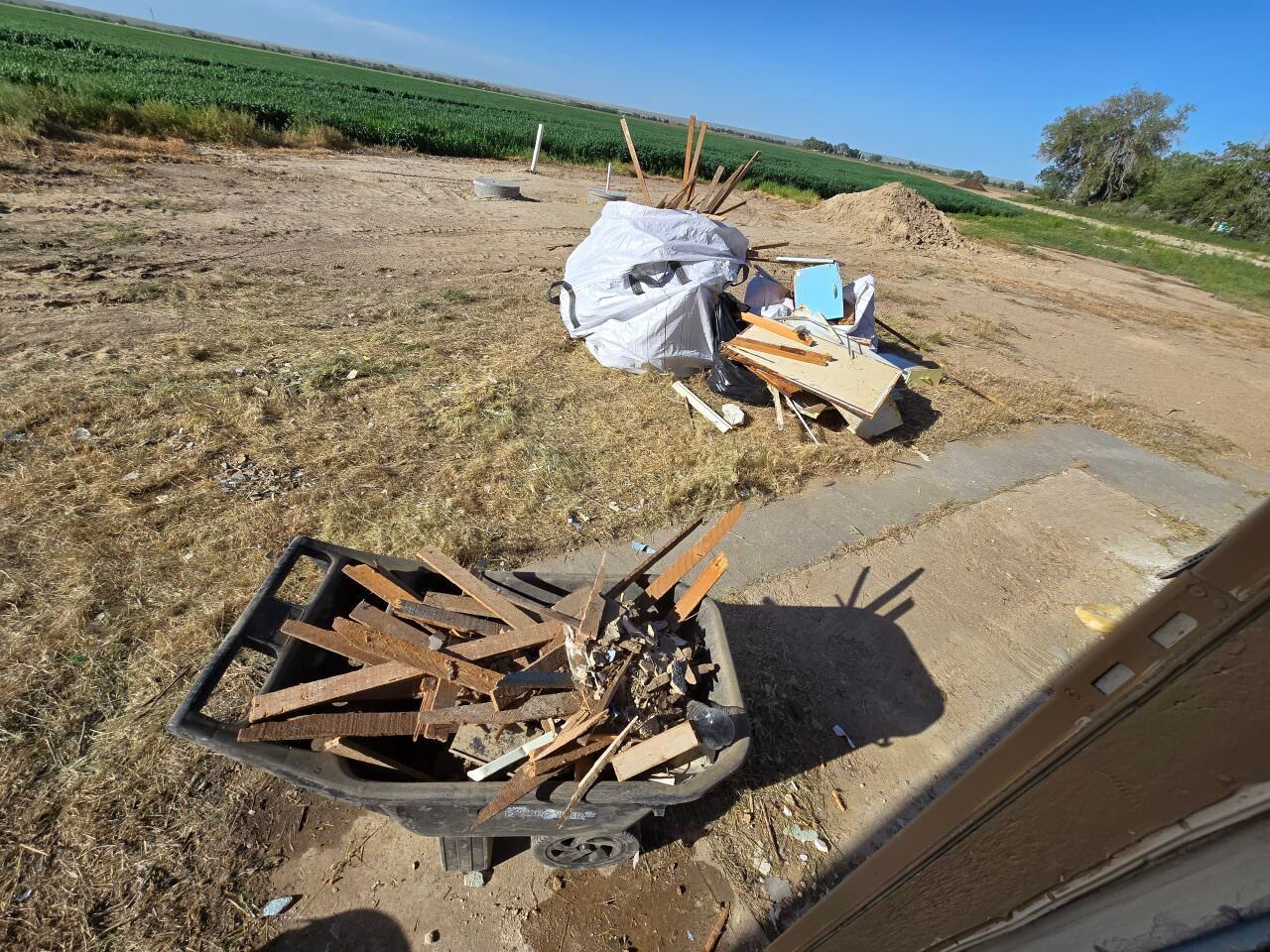 Debris and broken wood scattered beside a dirt road in a rural field under a blue sky