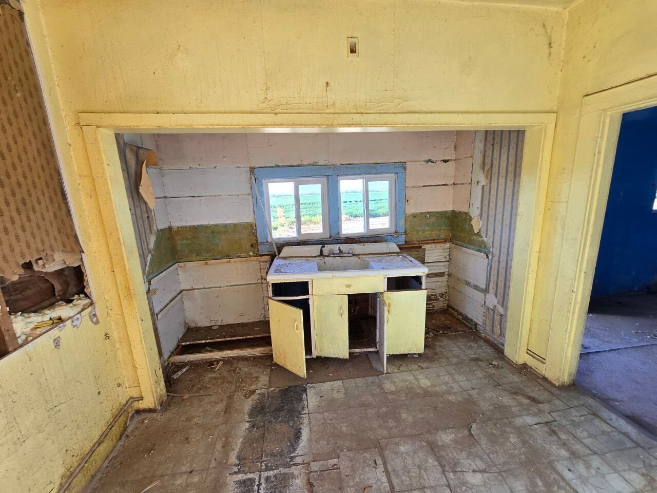 Dilapidated kitchen with peeling walls, old cabinets, and a small window.