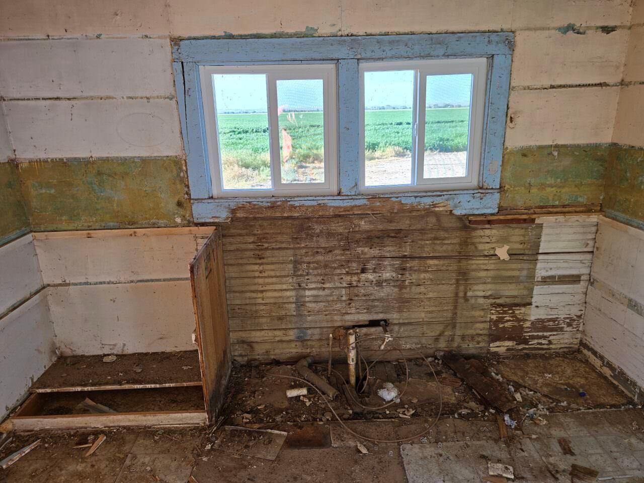 Deteriorated kitchen with peeling walls, a broken sink, and a small window above the counter.