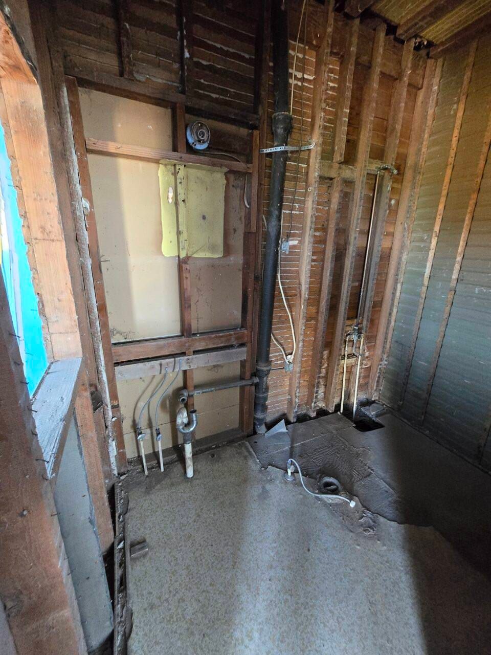 Unfinished interior wall with exposed wood studs, plumbing pipes, and electrical wiring in a room under construction
