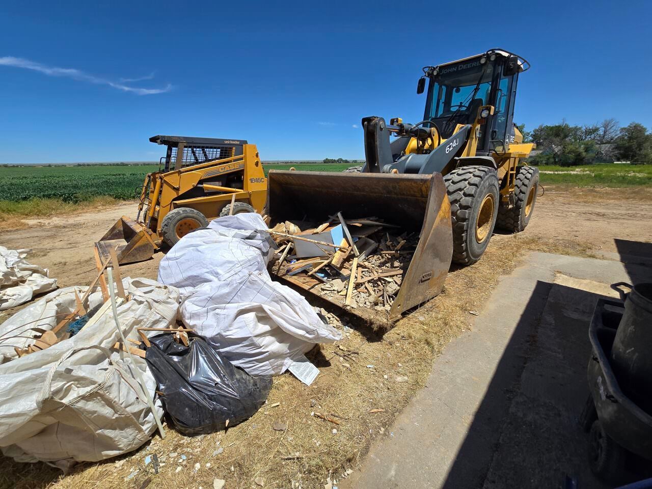 Yellow loader pushing debris beside white sandbags on a sunny construction site