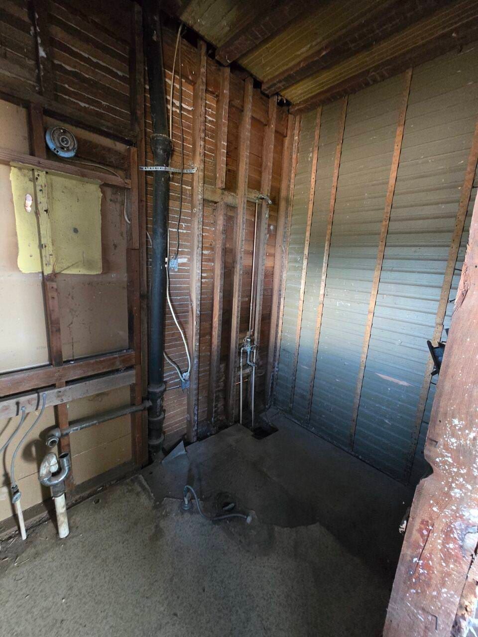 Renovation site with exposed wooden studs, insulation, wiring, and unfinished concrete floor.