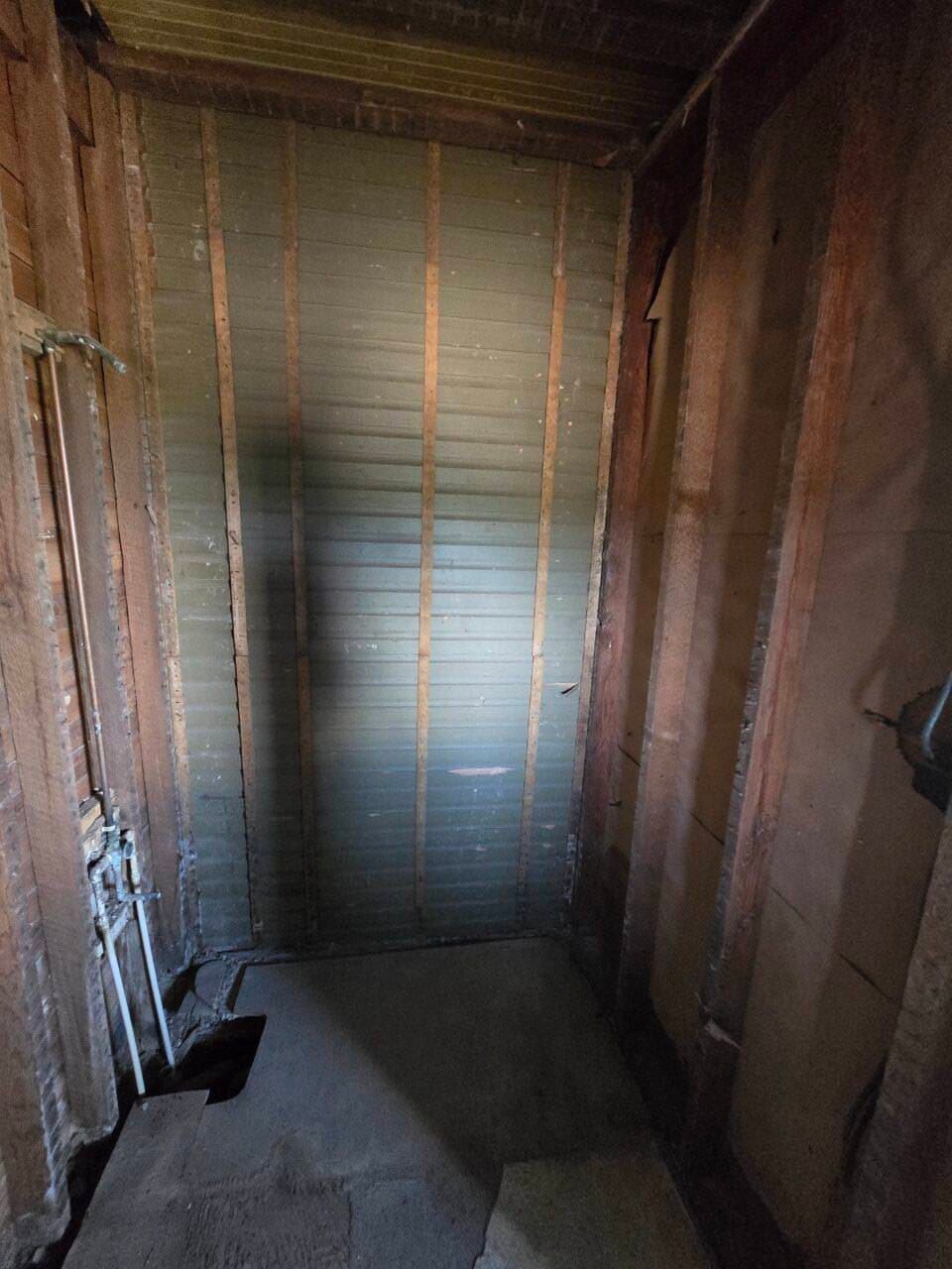 Narrow unfinished room with exposed framing, insulation, and a small window at the far end.