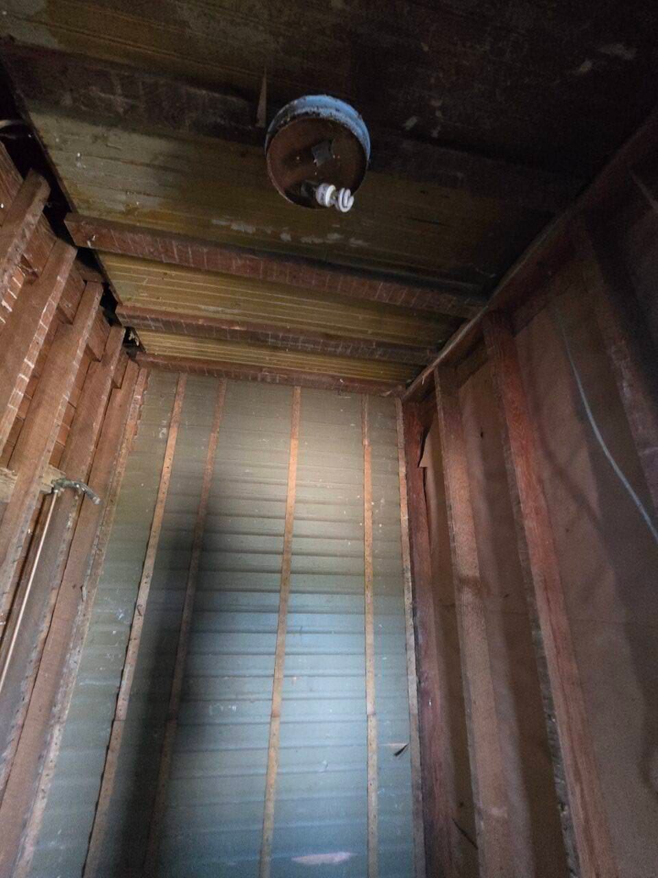 Old wooden elevator shaft interior with bare walls and a ceiling light fixture