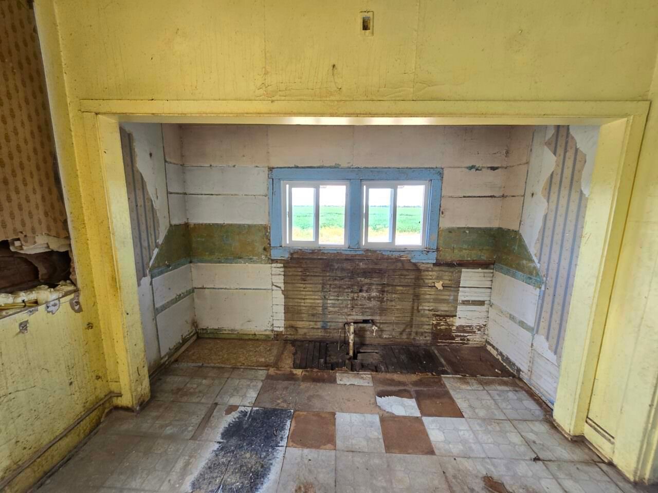 Empty yellow-walled kitchen with tiled floor, small window, and old sink counter.