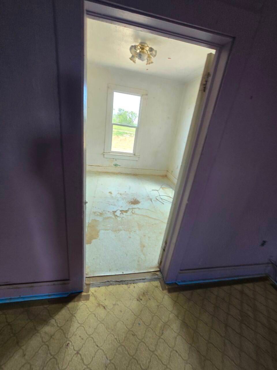 Open doorway into a bare white room with a window and ceiling light fixture.