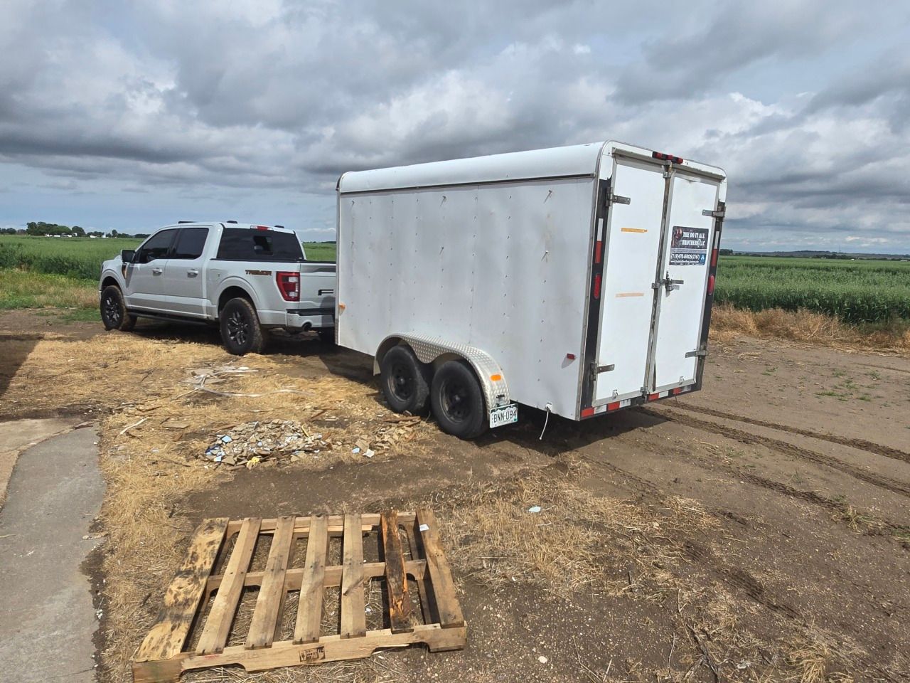 Silver SUV towing a white cargo trailer on a muddy dirt road under cloudy skies Silver SUV towing a white cargo trailer on a muddy dirt road under cloudy skies