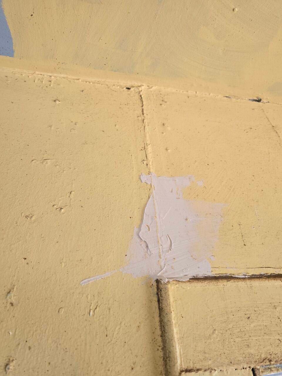 Close-up of a yellow painted wall with a chipped white patch and vertical seam