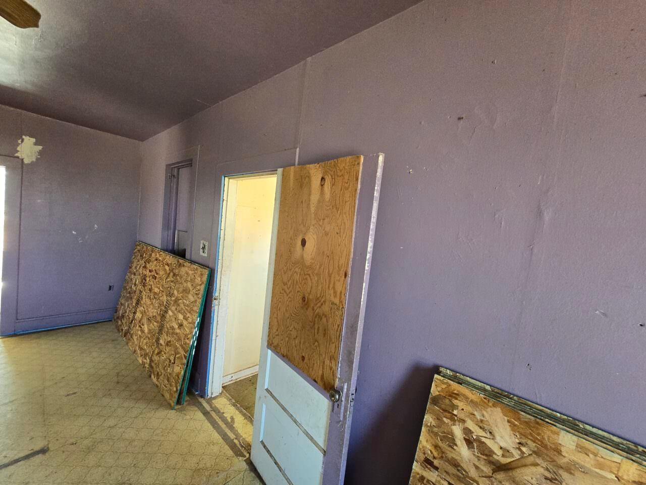 Unfinished room with purple walls, doorway, and plywood boards leaning against the wall