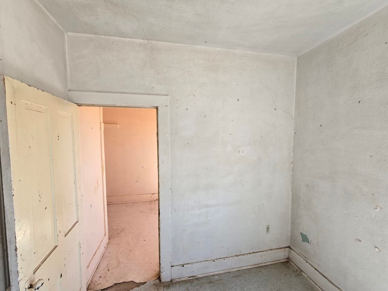 Empty white room with open doorways and bare walls, showing unfinished interior walls and floor.