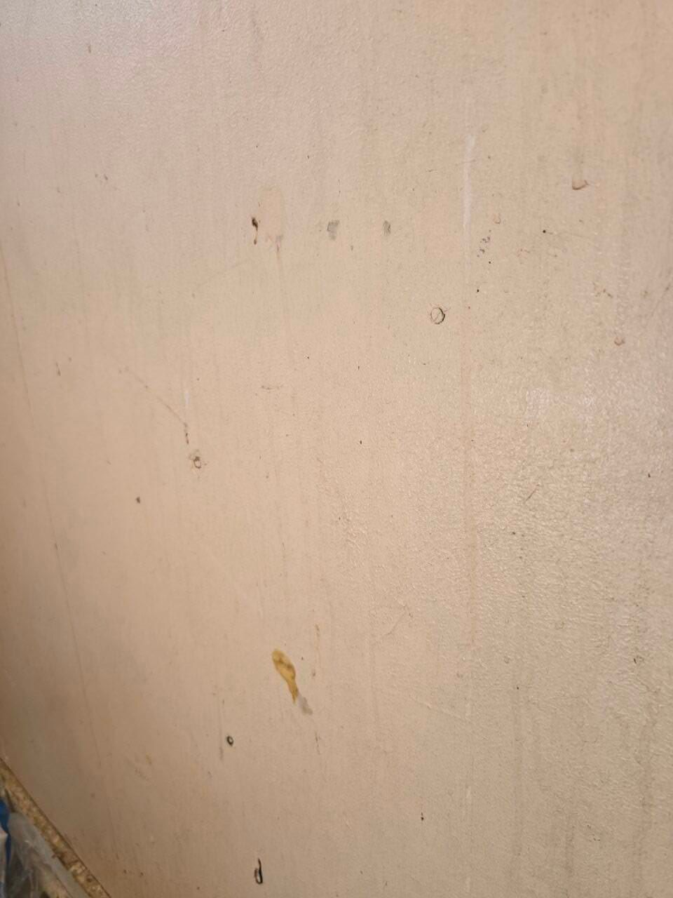 Close-up of a beige wall with small stains and scuff marks.