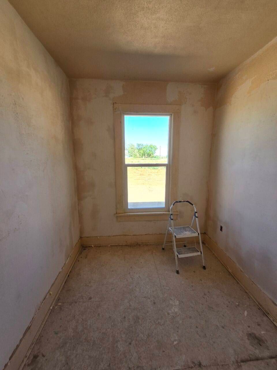 Narrow unfinished room with beige walls, a small window, and a step ladder on the floor. Narrow unfinished room with beige walls, a small window, and a step ladder on the floor.