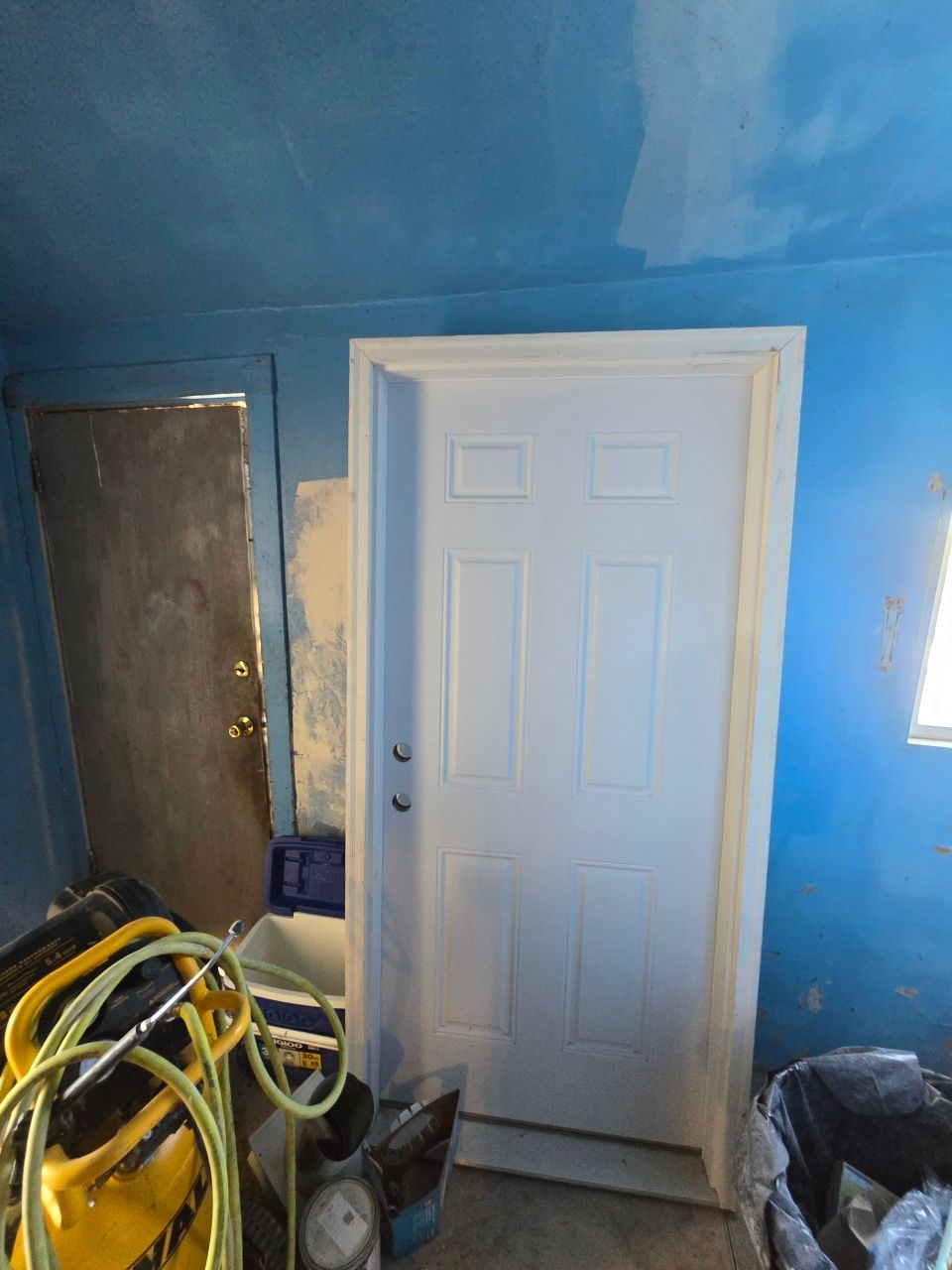 Blue room with white door, unfinished walls, and construction tools in the foreground. Blue room with white door, unfinished walls, and construction tools in the foreground.