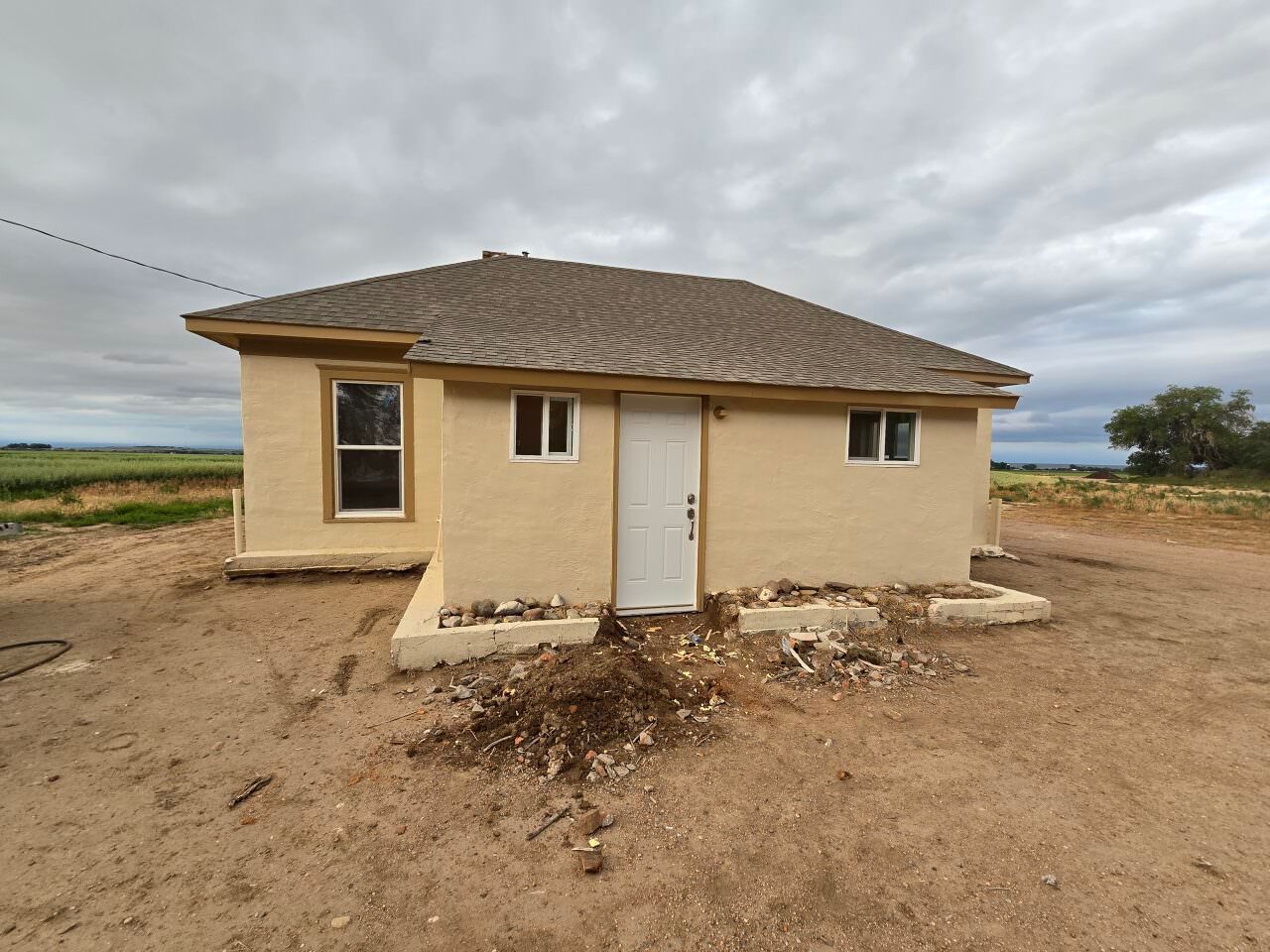 Small beige house with a white door in a dry, open rural landscape under cloudy skies