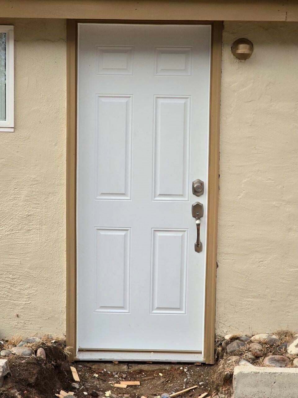 White front door with six panels and a deadbolt on a beige stucco house