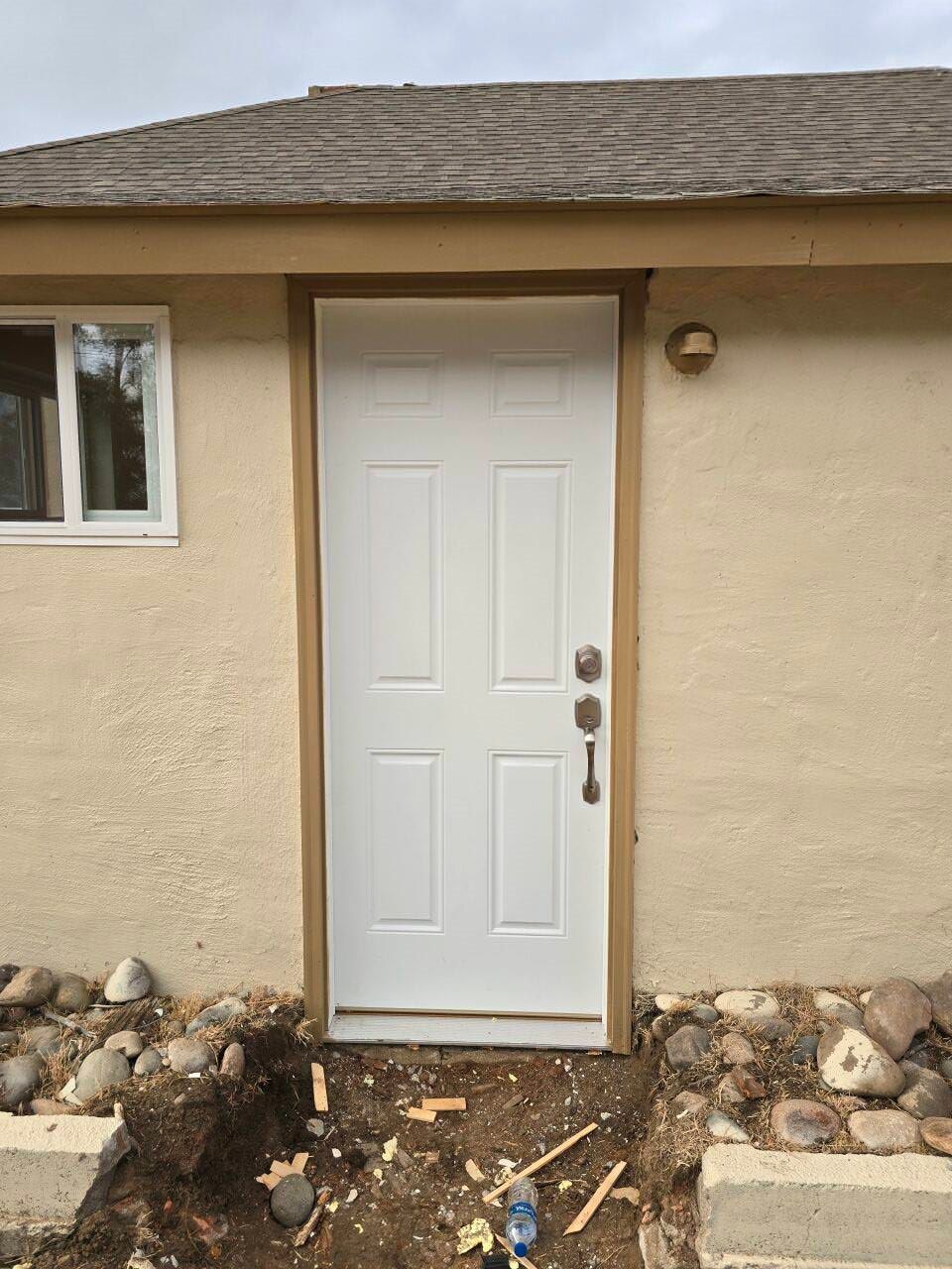 White front door on a beige house with rock landscaping and a small window to the left.