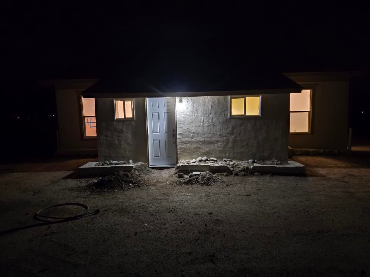 Small house at night with a lit front door and windows, surrounded by darkness. Small house at night with a lit front door and windows, surrounded by darkness.