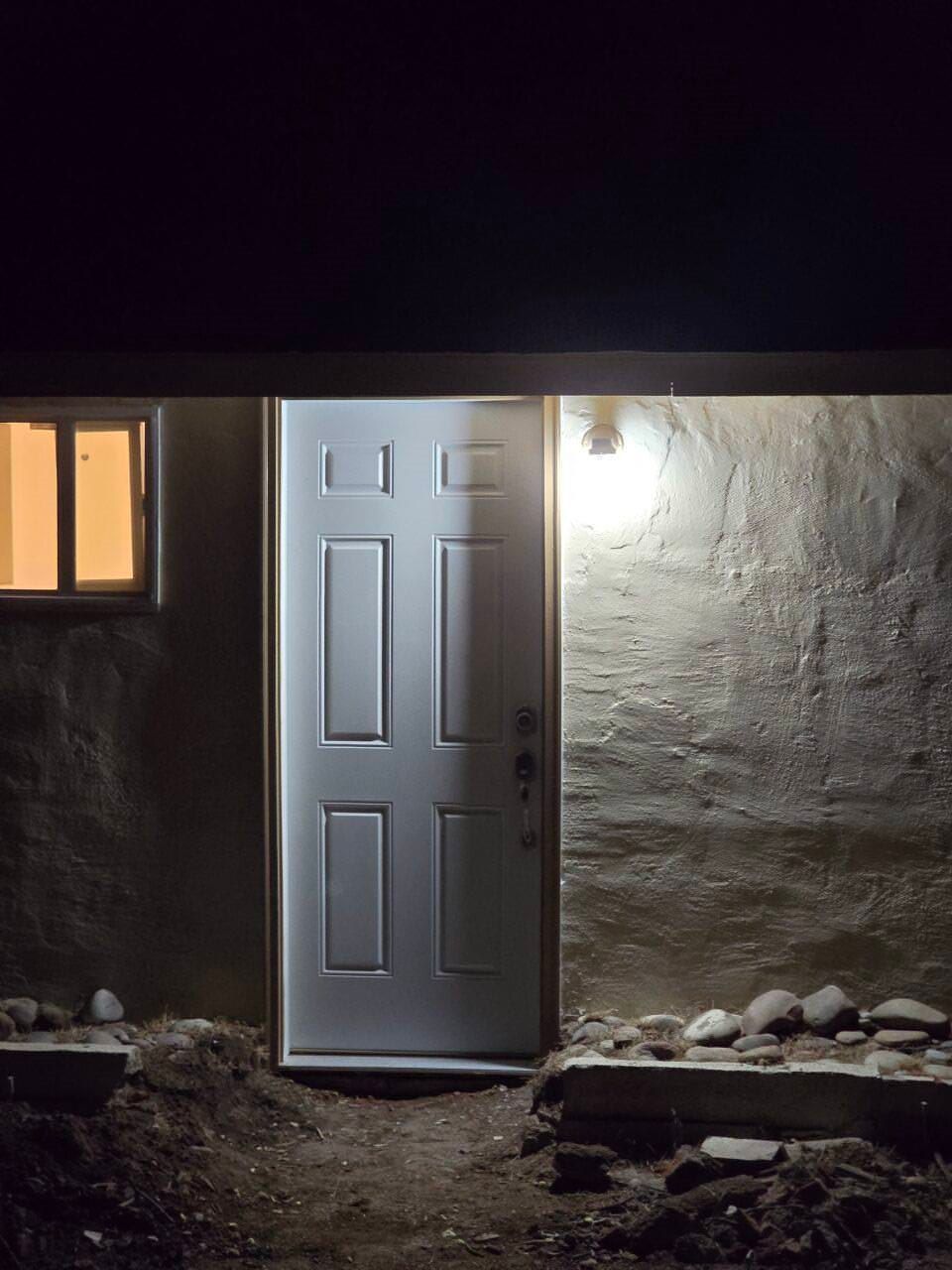 Front door of a house at night, lit by a porch light beside a small window.