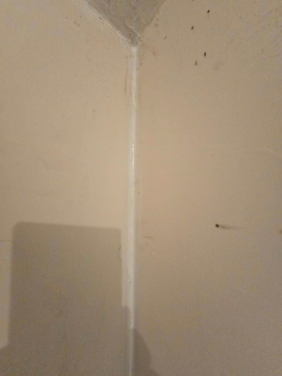Beige wall corner with a vertical white stripe and a gray rectangular object at bottom left Beige wall corner with a vertical white stripe and a gray rectangular object at bottom left