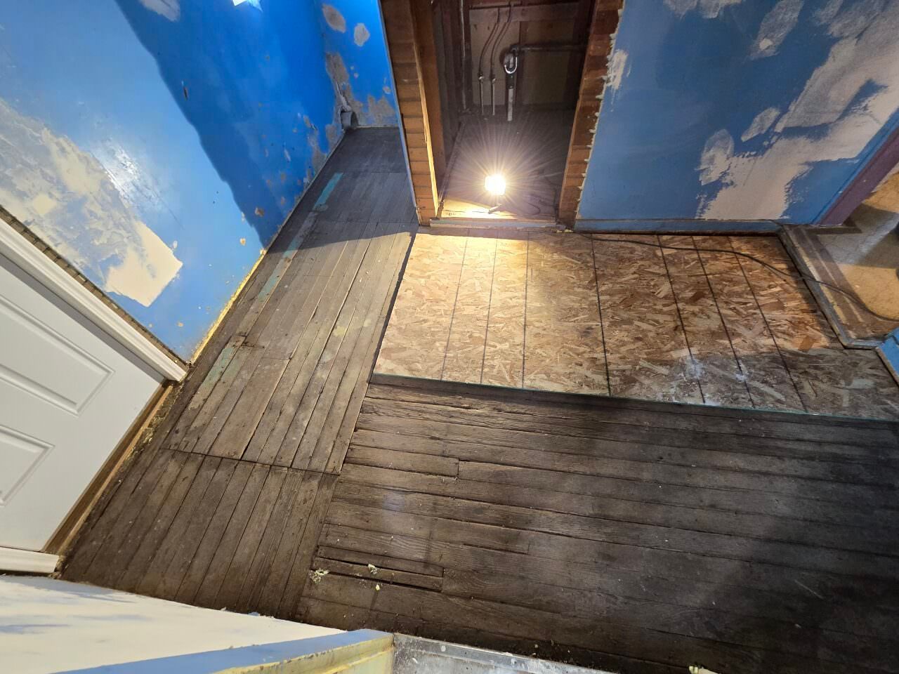 Dim attic hallway with blue sky mural walls, worn wood floor, and a lit doorway at the far end.