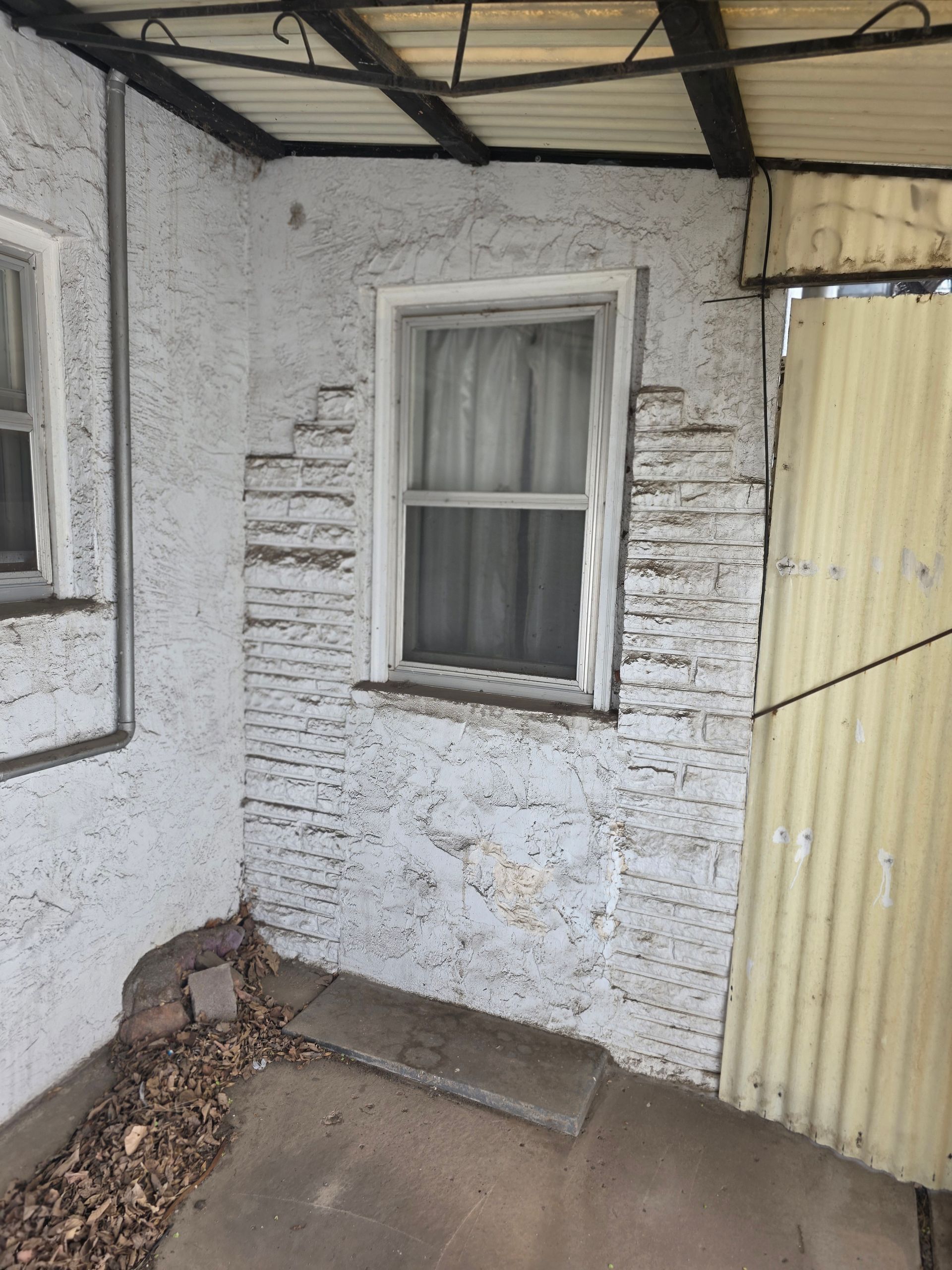 Small white exterior wall with window beside a yellow door and a concrete patio. Small white exterior wall with window beside a yellow door and a concrete patio.