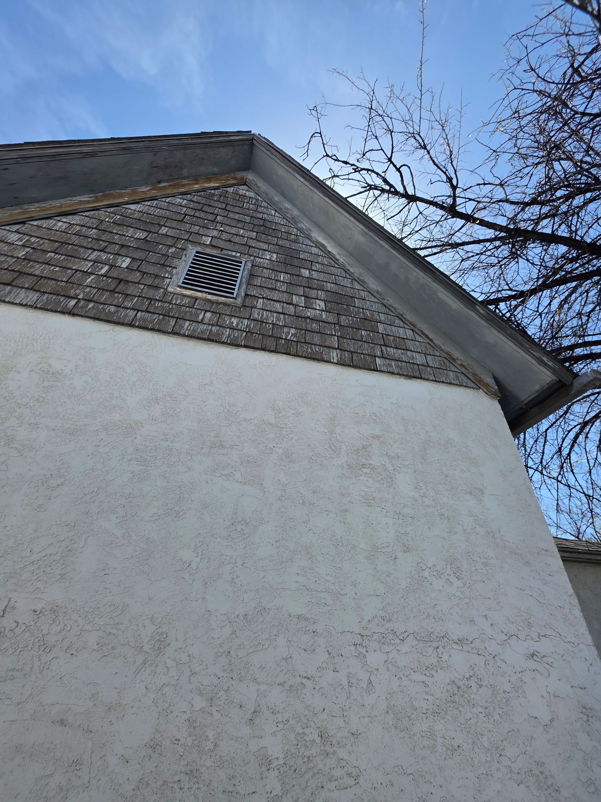 Low-angle view of a white stucco building wall and brick gable with a small vent against a blue sky Low-angle view of a white stucco building wall and brick gable with a small vent against a blue sky
