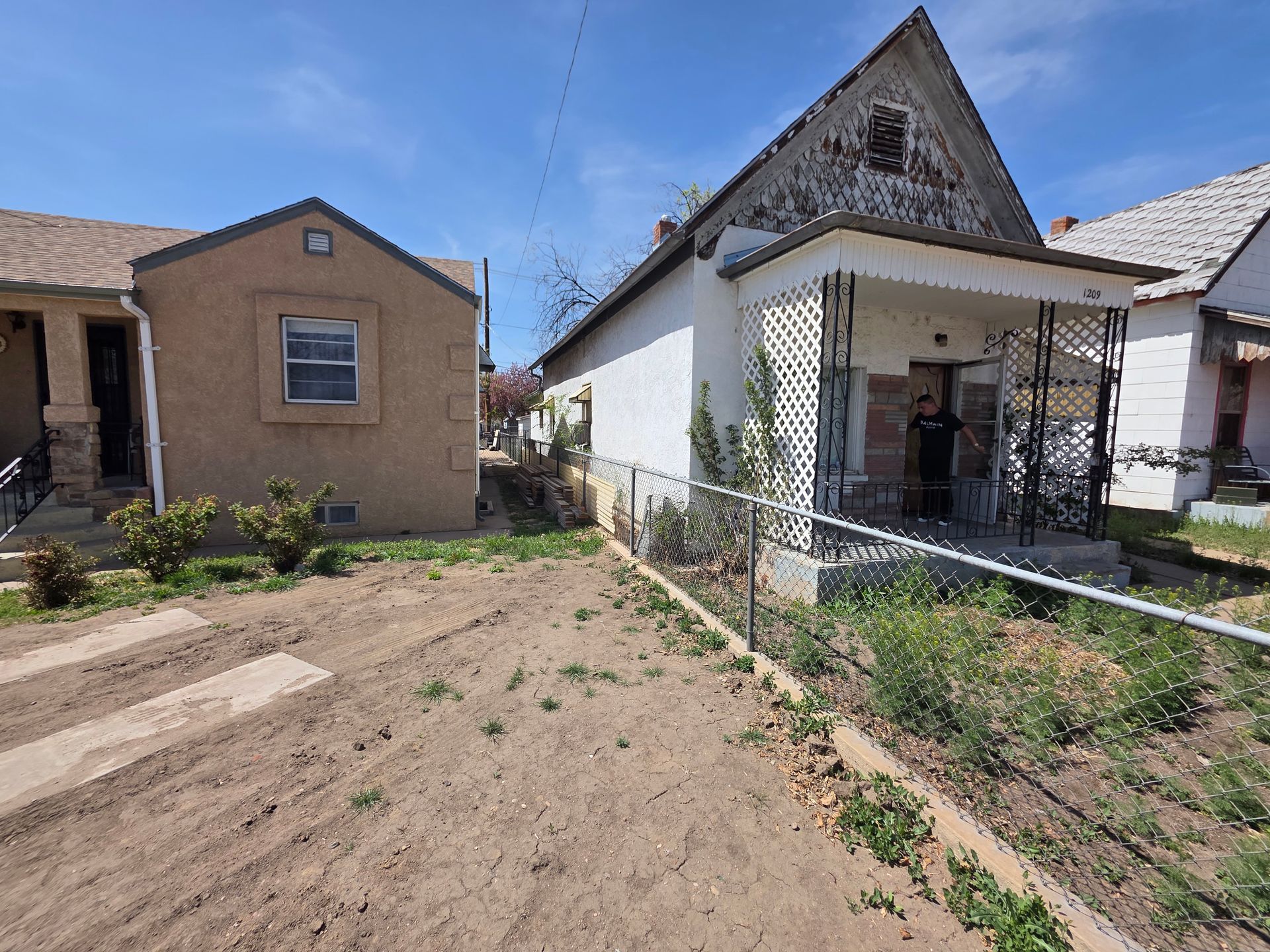 Front yards of two small houses, one with a white porch and fenced garden, under a clear blue sky Front yards of two small houses, one with a white porch and fenced garden, under a clear blue sky