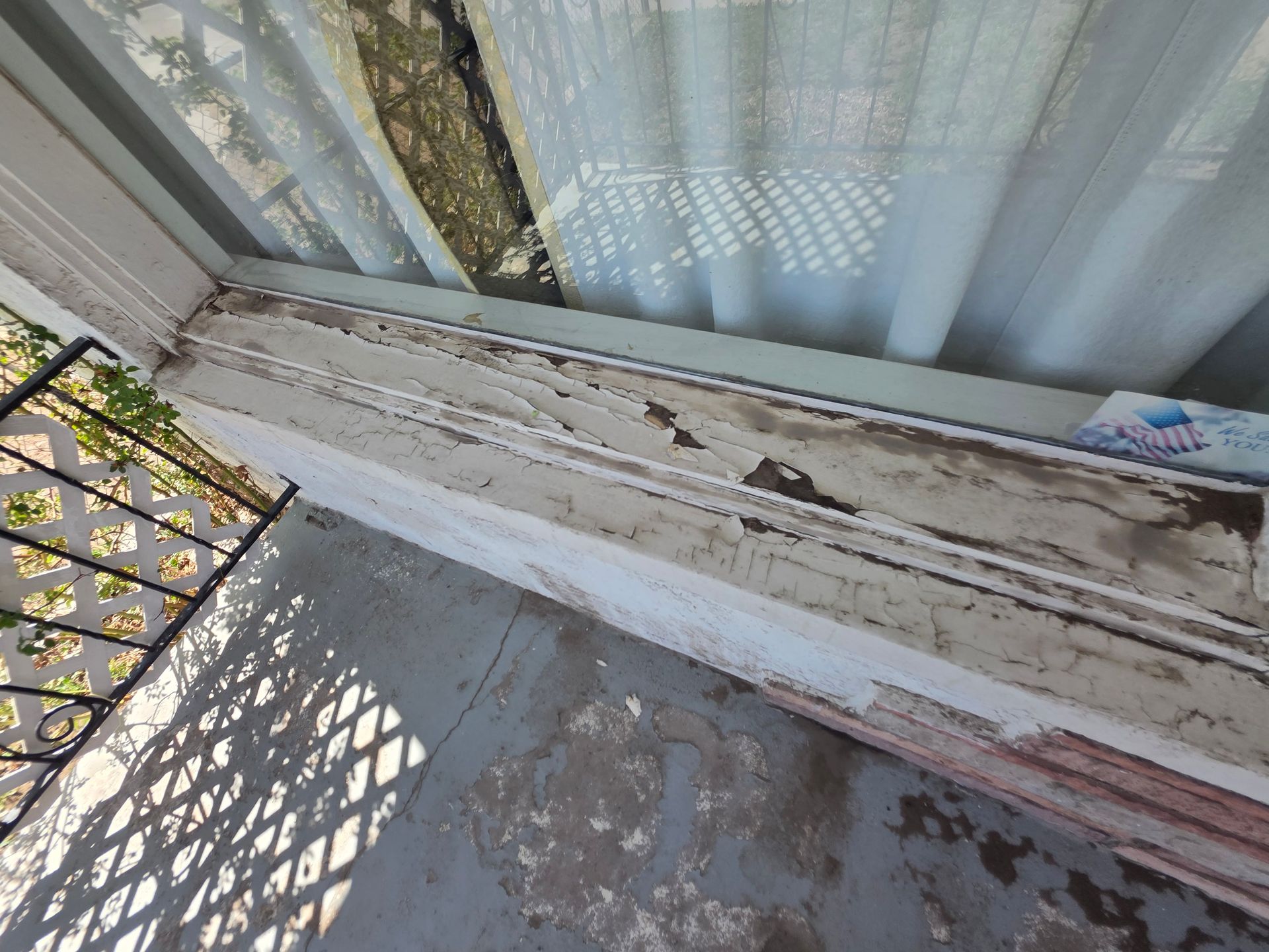 Peeling white-painted windowsill and balcony rail beside a curtain and metal railing Peeling white-painted windowsill and balcony rail beside a curtain and metal railing