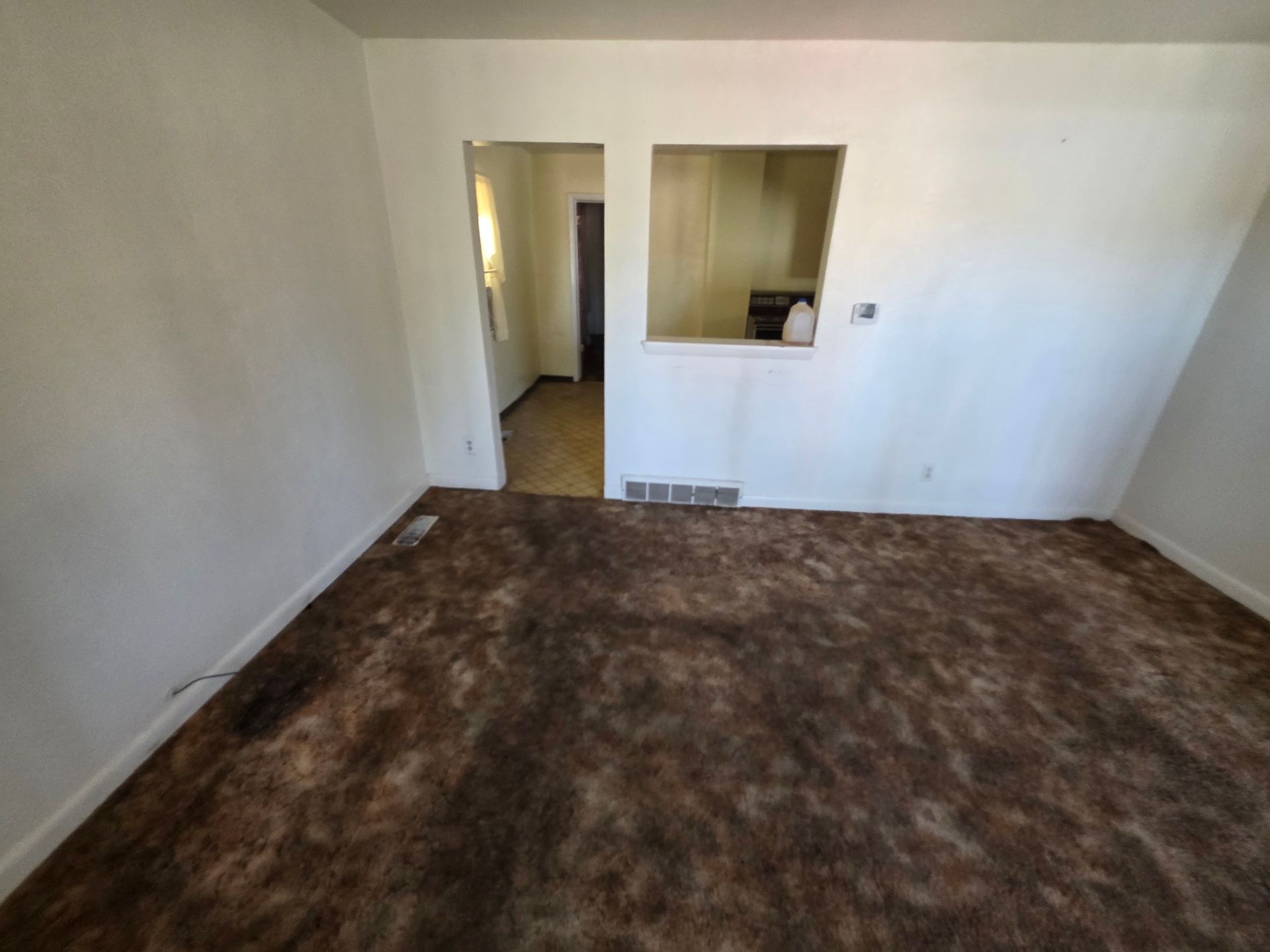 Empty room with brown carpet, white walls, and a pass-through opening to a hallway. Empty room with brown carpet, white walls, and a pass-through opening to a hallway.