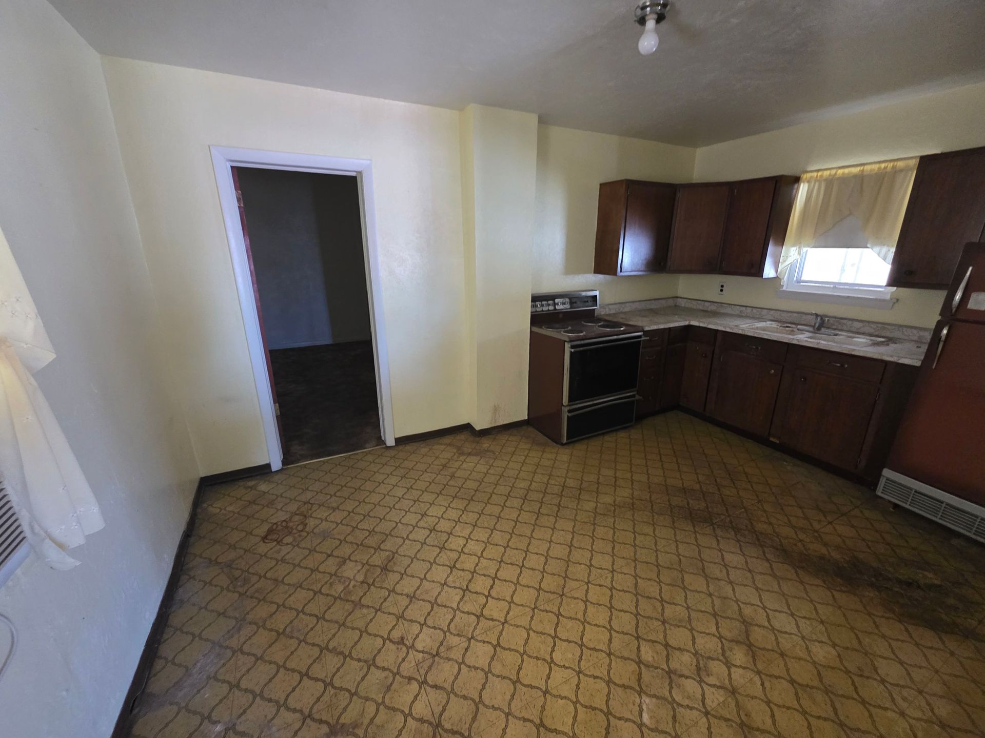 Empty kitchen with brown cabinets, patterned floor, and a doorway to another room. Empty kitchen with brown cabinets, patterned floor, and a doorway to another room.