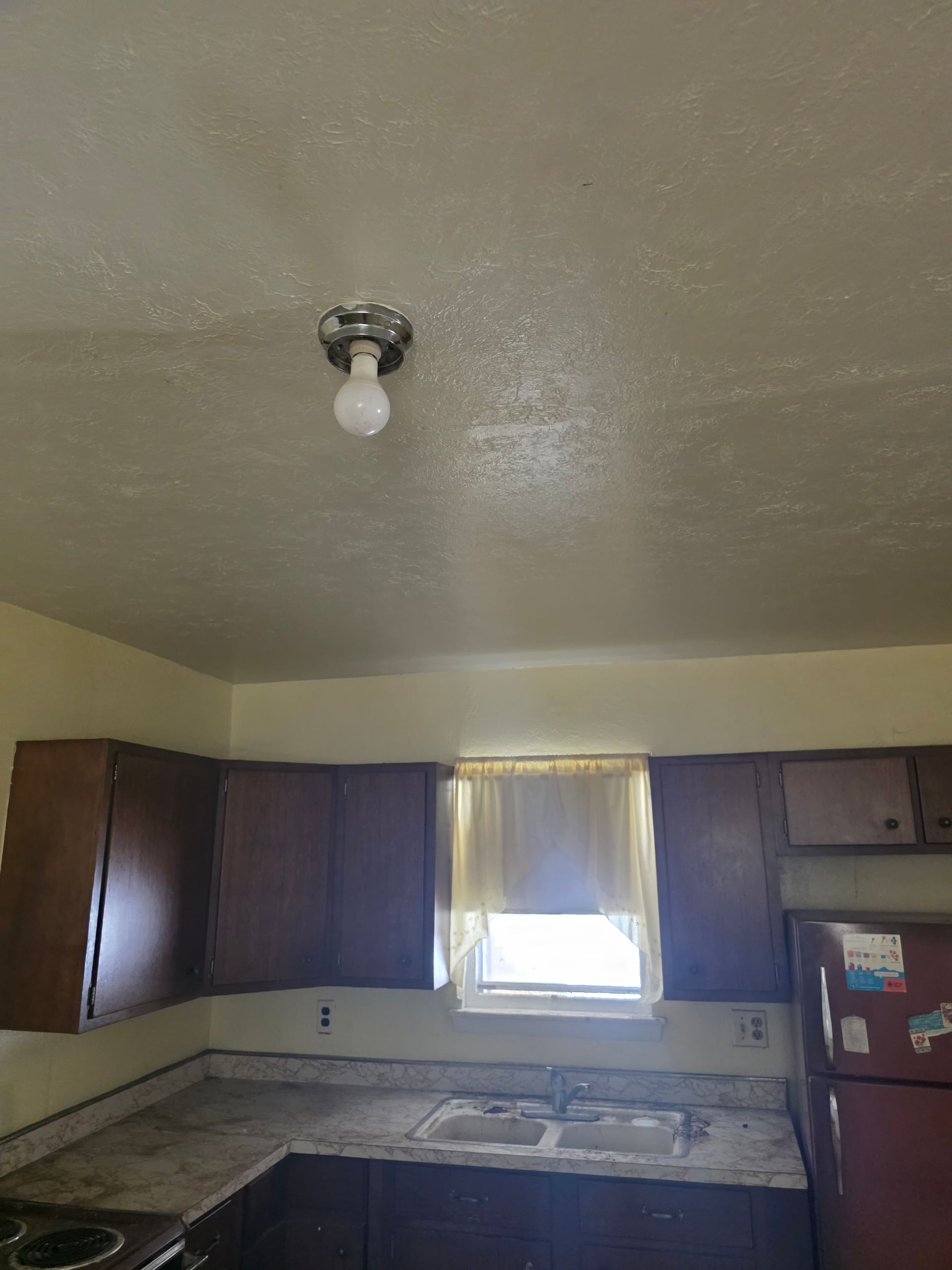 Small kitchen with dark cabinets, a window over the sink, and a bare ceiling light fixture. Small kitchen with dark cabinets, a window over the sink, and a bare ceiling light fixture.
