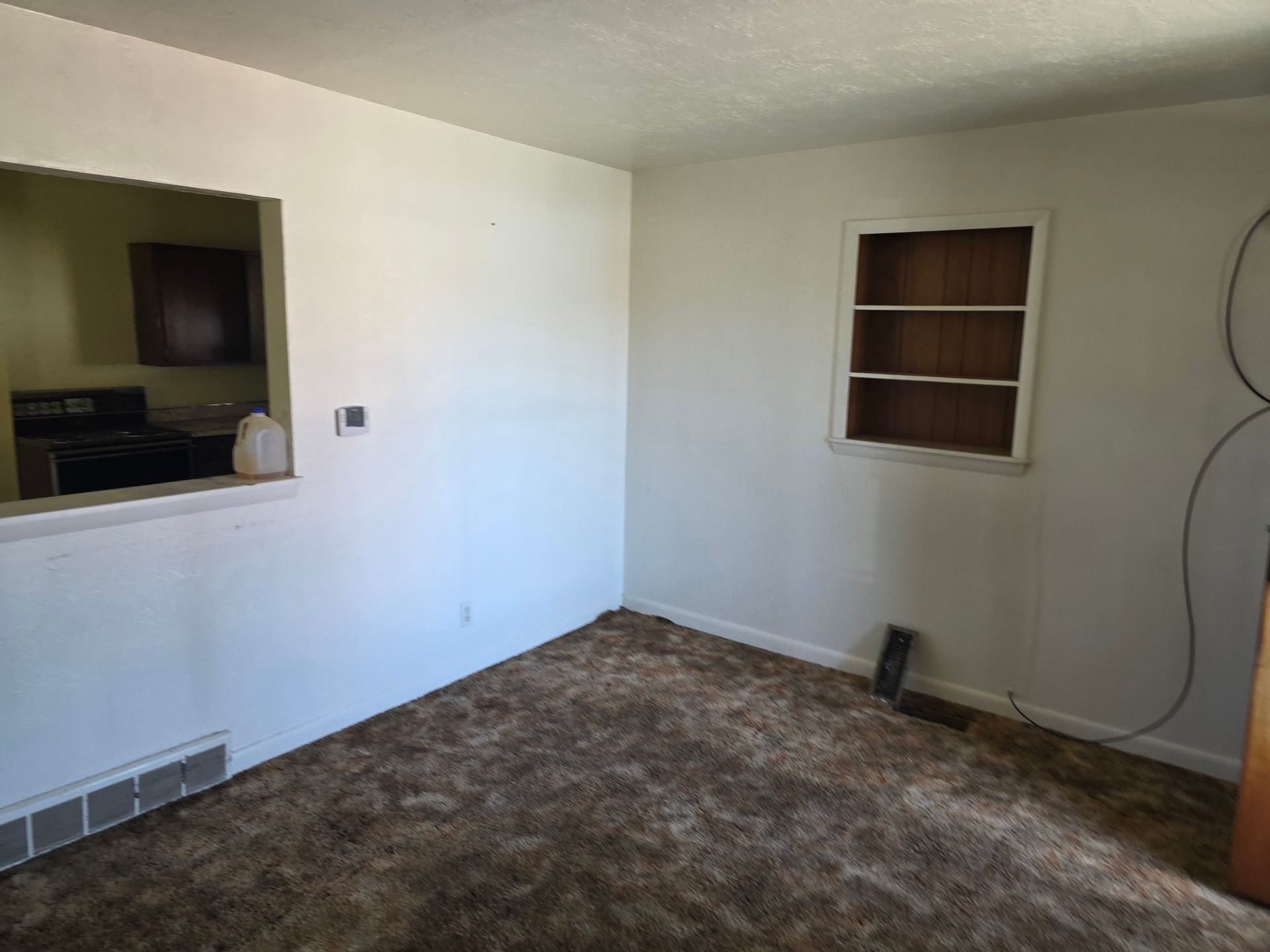 Empty beige room with brown carpet, a wall vent, and a small recessed shelf opening Empty beige room with brown carpet, a wall vent, and a small recessed shelf opening