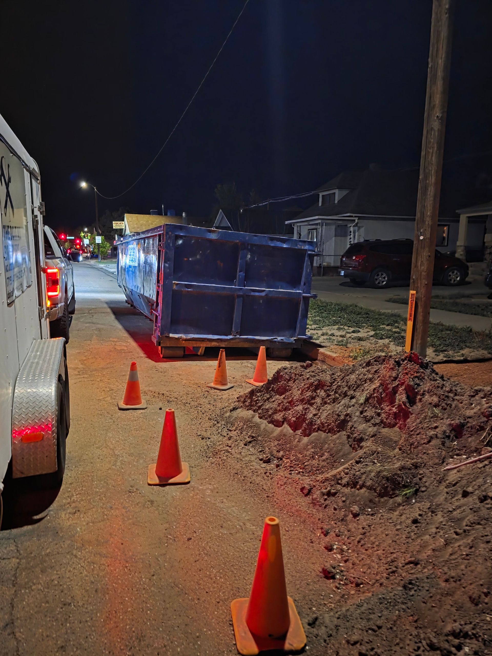 Night street with orange cones and a blue dumpster blocking a road repair area Night street with orange cones and a blue dumpster blocking a road repair area