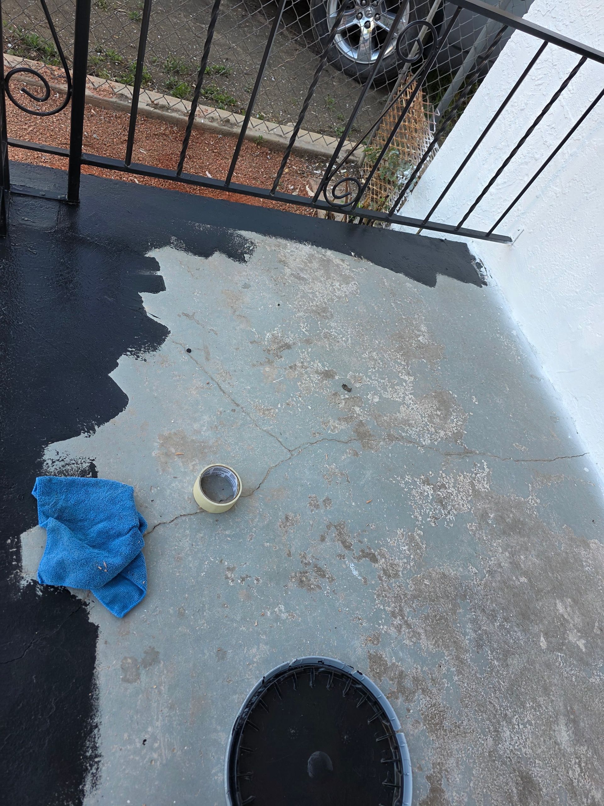 Small balcony with wet concrete, a drain, blue cloth, and a black metal railing. Small balcony with wet concrete, a drain, blue cloth, and a black metal railing.