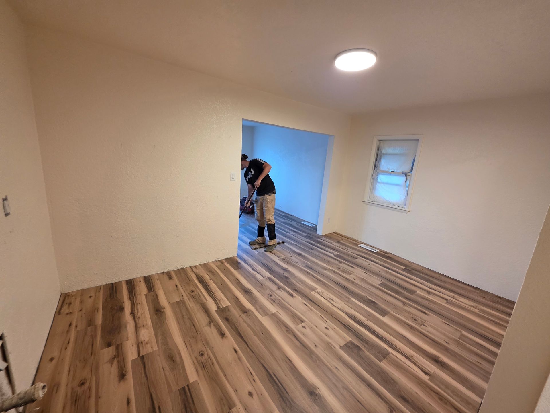 Empty room with wood flooring, white walls, and a person working near the open doorway. Empty room with wood flooring, white walls, and a person working near the open doorway.