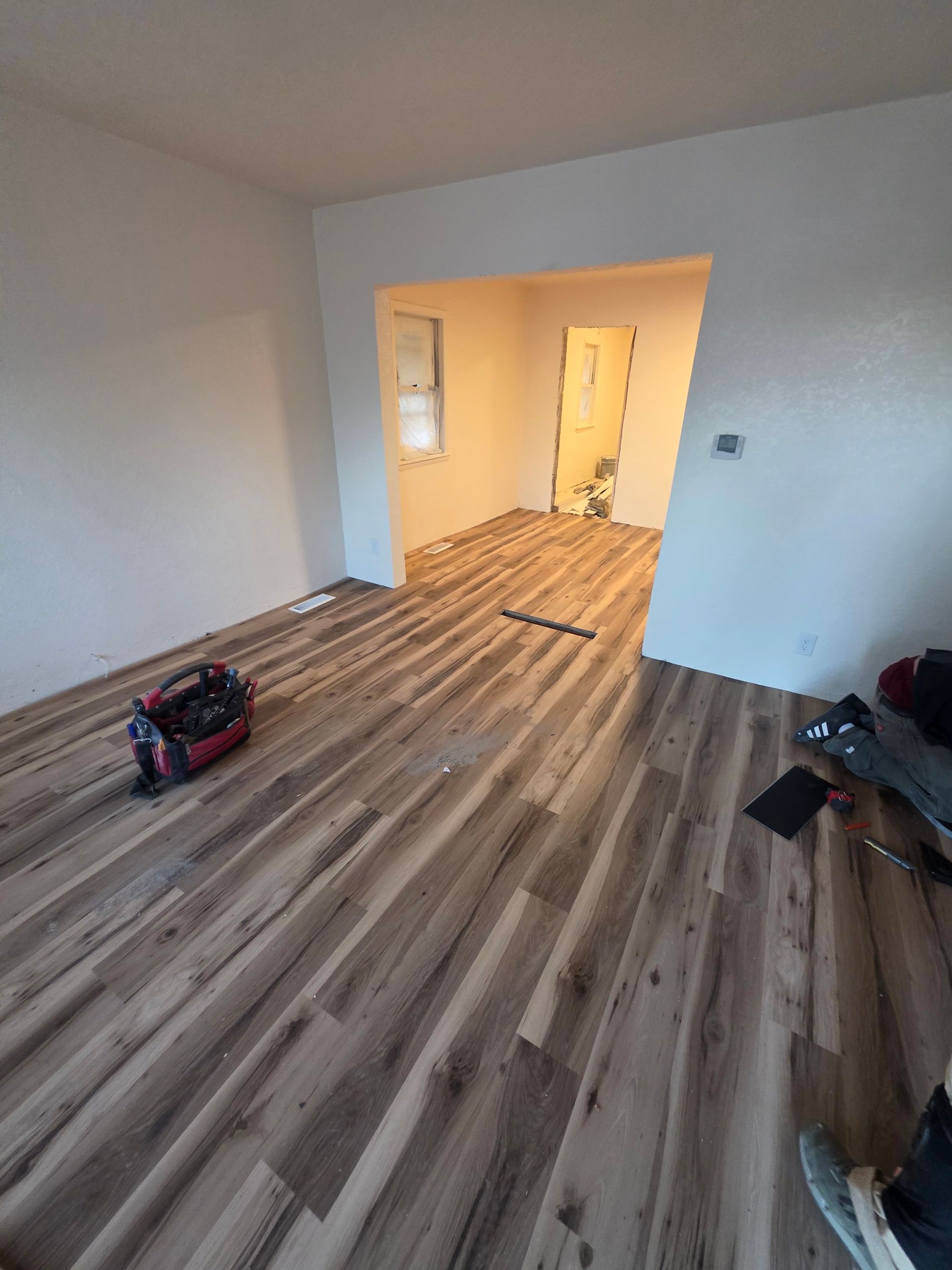 Empty room with wood-look flooring, white walls, and a doorway to a lit hallway. Empty room with wood-look flooring, white walls, and a doorway to a lit hallway.