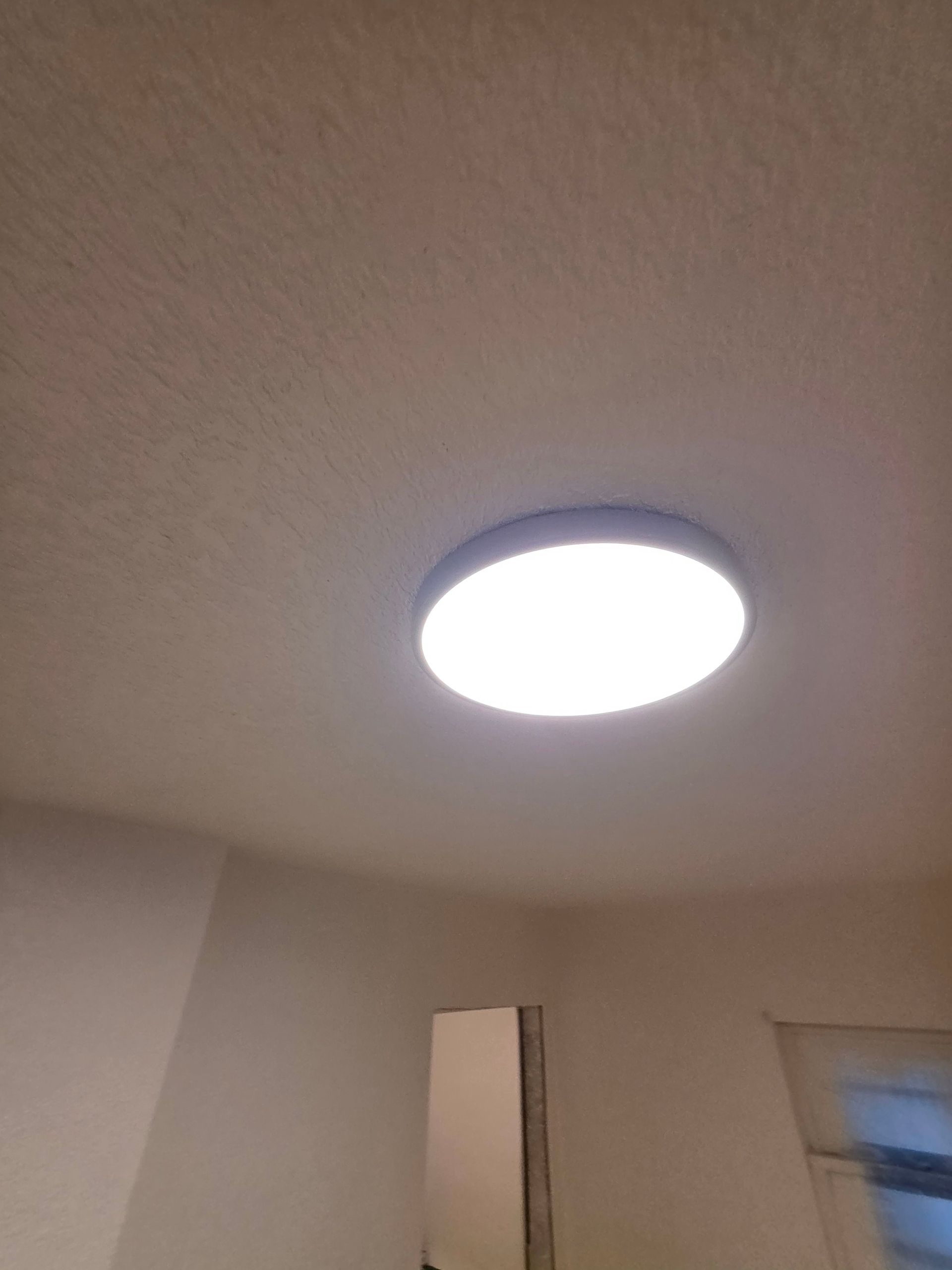 Ceiling light on a beige ceiling in an indoor room, with a doorway and window below. Ceiling light on a beige ceiling in an indoor room, with a doorway and window below.
