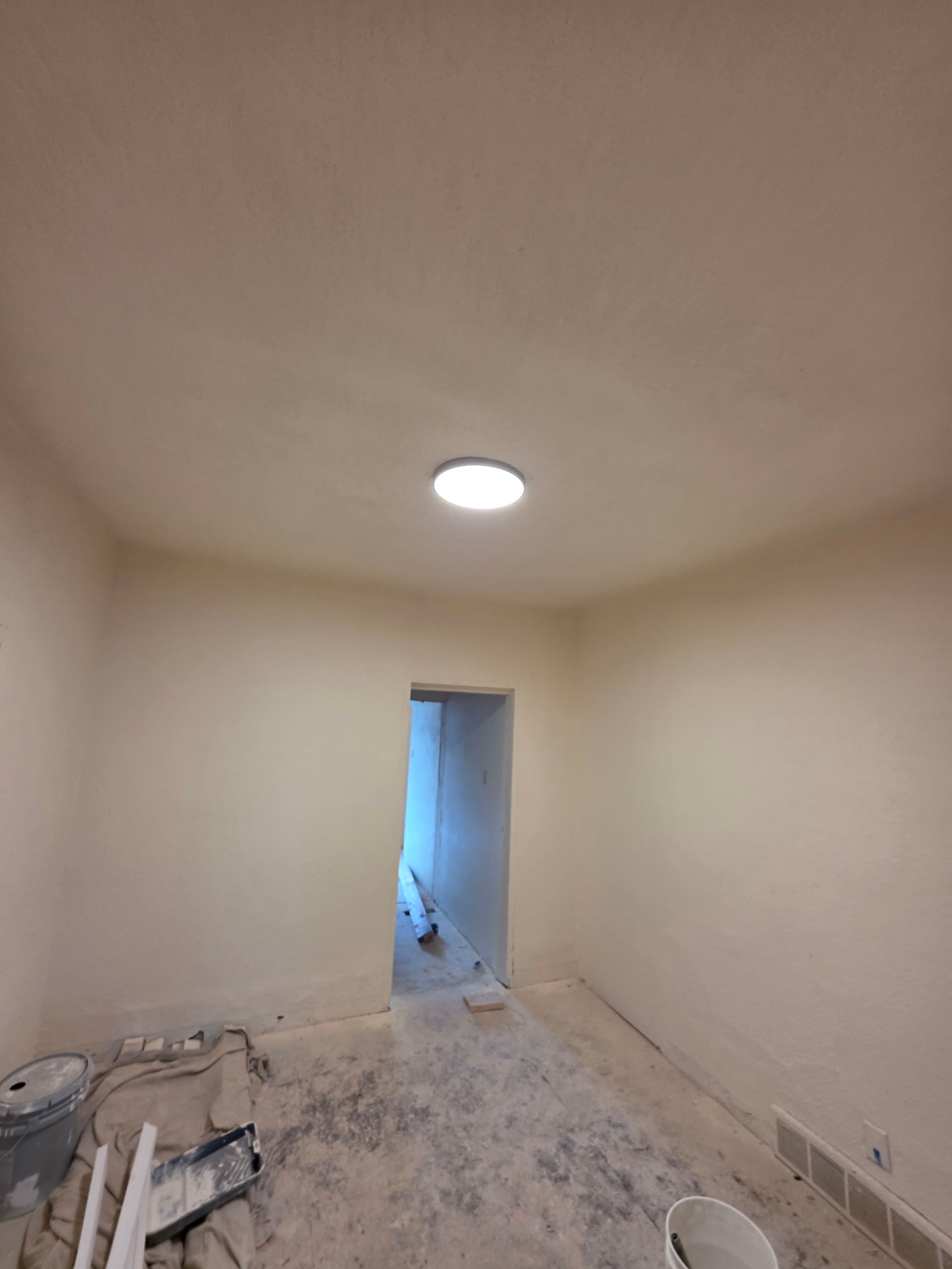 Empty beige room under renovation with unfinished floor and a doorway to a blue-lit hall